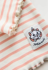 Material cu dungi în crem și roz deschis, cu margini ondulate. Prezintă un patch cu o pisică de desene animate și numele "Marie" scris în cursiv.