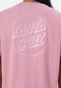 Korte roze t-shirt met een groot, lichtroze "SANTA CRUZ" logo in een vet lettertype, met een cirkelvormige omtrek en "SKATEBOARDS" eronder.