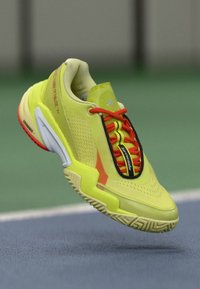 Neon yellow athletic shoe with red and black accents, mesh upper, textured sole, and visible lacing system, designed for performance.