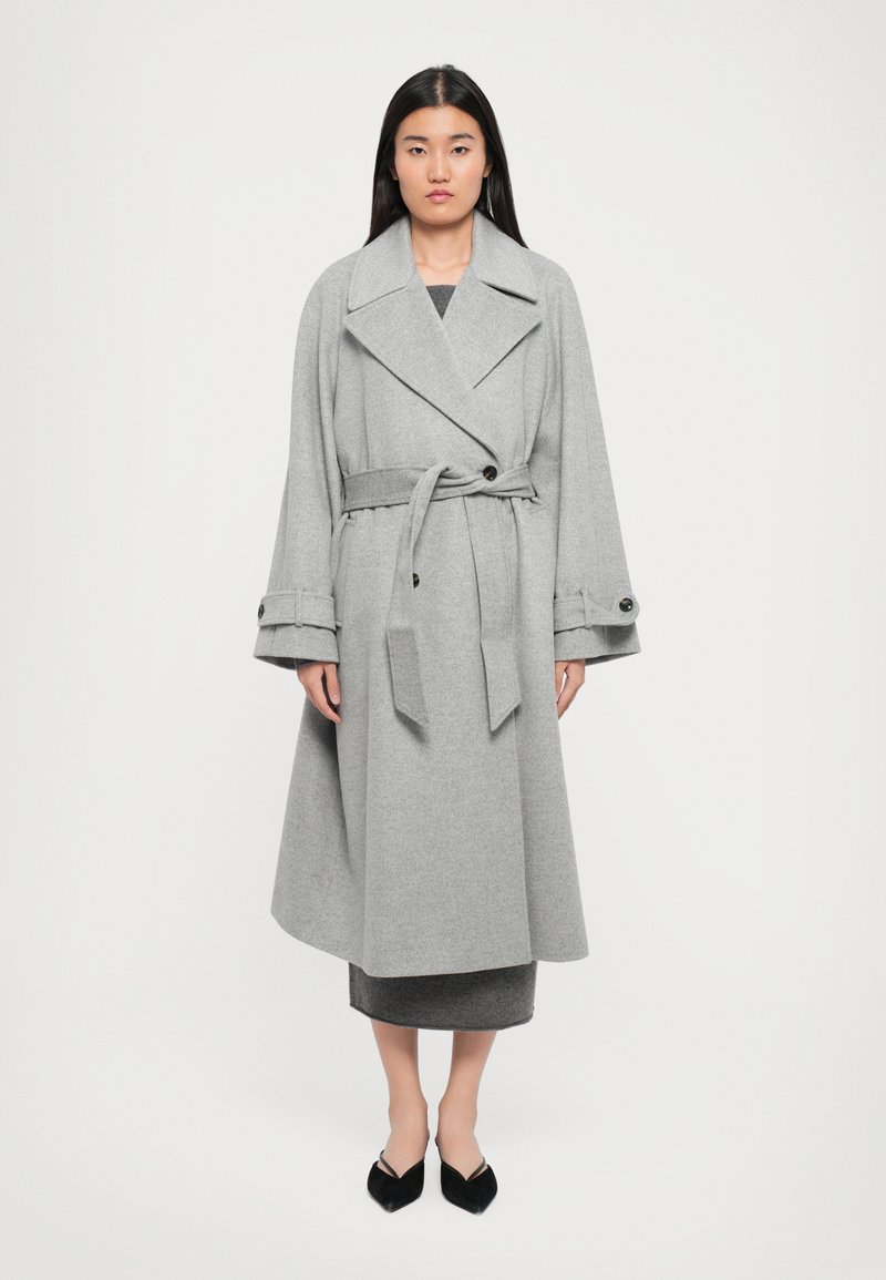 Grå ulltrenchcoat med breda ärmar, stor krage och matchande bälte. Har knapppdetaljer på ärmsluten.