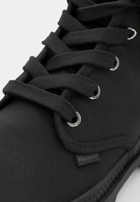 Sort høj-top sneaker med tekstureret stof, flade snørebånd, sølvøjer og et lille logoskilt på siden.