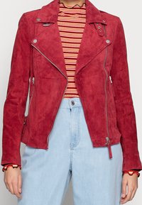 Červená nubuková moto bunda se stříbrnými zipy a patentkami, s přiléhavým střihem a mírně texturovaným povrchem, kombinovaná s pruhovanou košilí.