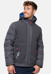 Veste isolée grise avec une capuche bleue, dotée de coutures verticales, de poches zippées et d'accents de cordon rouge. Détail de logo embossé.