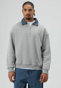 Lichtgrijze sweater met een denim kraag, een halve ritssluiting en geribbelde boorden. Heeft een relaxte pasvorm en een zachte textuur.