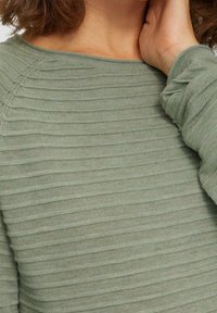 Ljusgrön ribbad stickad topp med texturerade ränder och avslappnad halsringning, med långa ärmar och samlade manschetter.