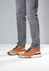 Nauhalliset tennarit oranssin, harmaan ja mustan nupukkinahkasyistä, joissa paksu valkoinen pohja. Kenkässä verkkomateriaalipaneeleja ja kontrastivärisiä yksityiskohtia.