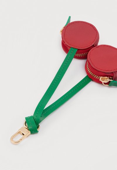Κόκκινα διπλά κυκλικά πορτοφόλια με χρυσά φερμουάρ συνδεδεμένα με πράσινα λουριά. Υφή λείου δέρματος, με μεταλλικό χρυσό κούμπωμα στο τέλος.