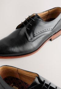 Black leather dress shoes with a smooth finish, pointed toe, and perforated detailing. Brown sole with a beige interior lining.