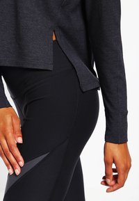 Maglia sportiva a maniche lunghe grigio scuro con spacchi laterali abbinata a leggings neri con un motivo grigio. Tessuto morbido.
