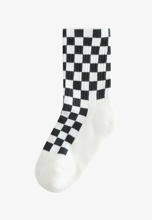 Bijele čarape s odvažnim crno-bijelim kariranim uzorkom, izrađene od mekog materijala s rebrastom teksturom, dizajnirane za udobnost.
