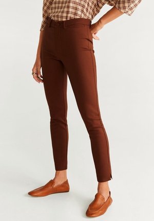 Pantalon marron slim jusqu'à la cheville, associé à des chaussures marron en cuir à enfiler, porté avec une chemise à carreaux rentrée.