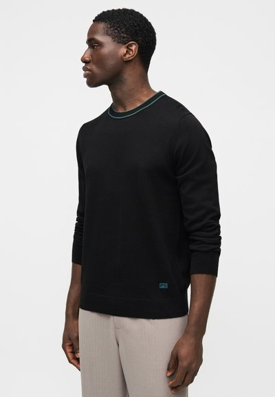 Čierny pletený sveter s rebrovaným okrúhlym výstrihom so zeleným akcentom. Priliehavé rukávy a malé logo na spodnom leme.