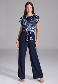 Combinaison bleu marine avec un haut à motifs et des accents floraux bleus, taille nouée. Tissu doux, design à jambe large et manches courtes.