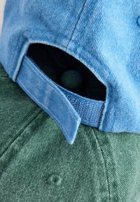 Deux casquettes empilées, une bleue et une verte. La casquette bleue présente une texture en jean avec une sangle ; la casquette verte est en tissu pelucheux.