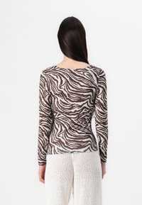 Pikendusega sarka, millel on pruun ja valge zebra triibuline muster, sujuva tekstuuriga ja ümmarguse kaelusega.