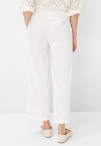 Weiße weit geschnittene Hosen mit besticktem Saum. Der Stoff scheint leicht und mit einer glatten Textur versehen zu sein. Kombiniert mit beigen Ballerinas.