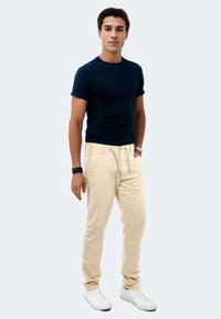 Dunkelblaues, tailliertes T-Shirt kombiniert mit hellbeigen Drawstring-Hosen und weißen Sneakers vor einem schlichten Hintergrund.