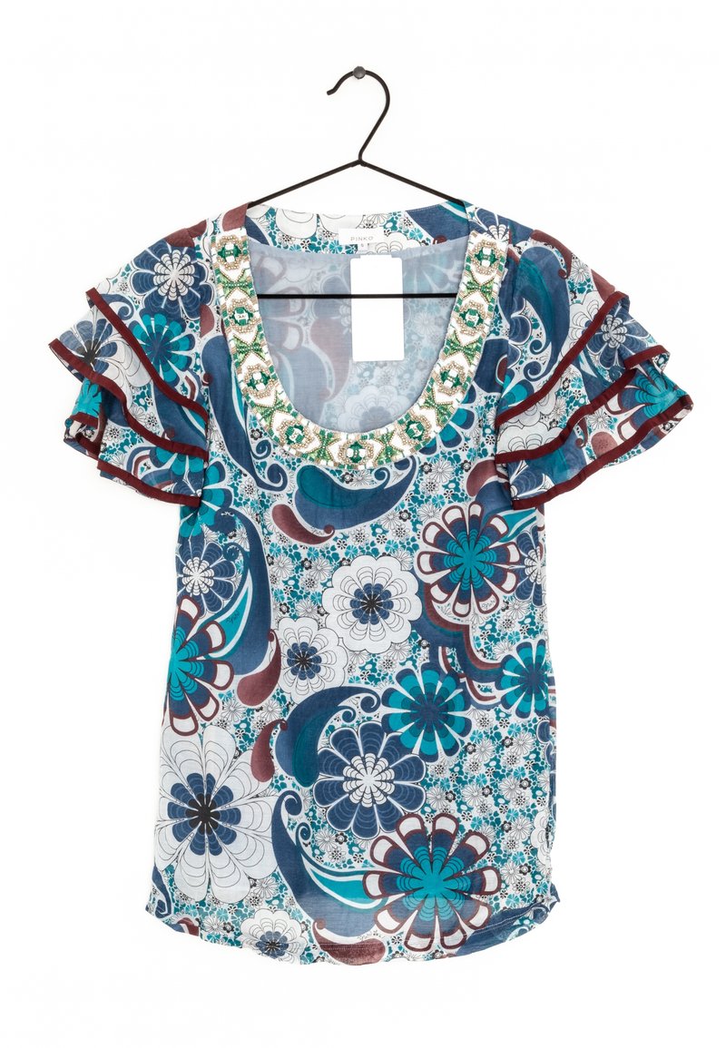 Blouse à motif floral avec un col rond, des manches courtes à volants et des accents de perles vertes autour du décolleté. Les couleurs incluent le turquoise, le bleu et le bordeaux.