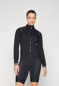 Svart sykkeljakke med høy krage, glidelås foran og grå aksenter. Lett og tettsittende design med lange ermer. Svart sykkelshorts nedenfor.