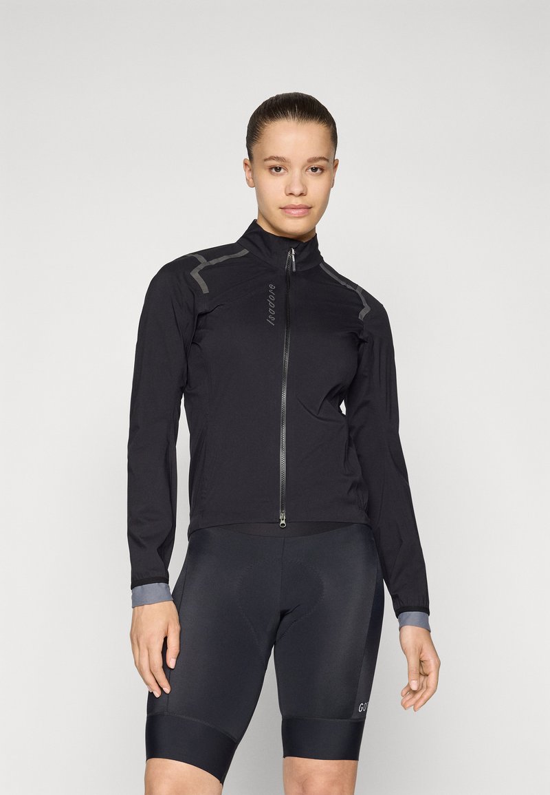 Svart sykkeljakke med høy krage, glidelås foran og grå aksenter. Lett og tettsittende design med lange ermer. Svart sykkelshorts nedenfor.