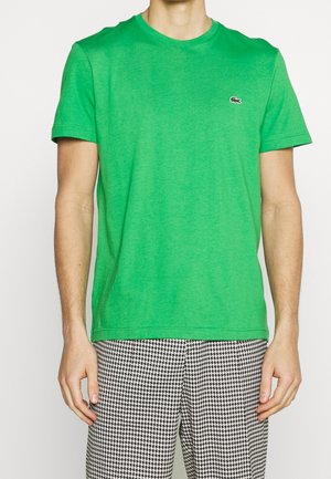 Uomo che indossa una maglietta a maniche corte di un brillante verde con un piccolo logo di coccodrillo e pantaloni a quadri bianco e nero.