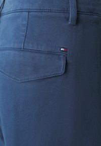 Pantaloni di cotone blu scuro con una tasca posteriore e un piccolo logo di marca in rosso, bianco e blu, texture liscia e vestibilità su misura.