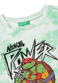 Camiseta verde tie-dye con un dibujo de una tortuga de dibujos animados sosteniendo armas, con el texto "PODER NINJA" en negrita y gráficos negros. Material de algodón suave.