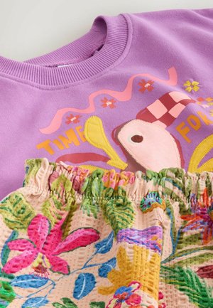 Vyšninio atspalvio džemperis su spalvingo paukščio grafika ir tekstu, derinamas su po kaklo linija susmulkintu audiniu su gėlėmis.