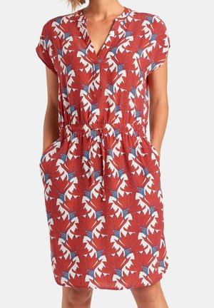 Vrouw draagt een knielange jurk met een rood bloemenpatroon, V-hals, korte mouwen en een elastische tailleband met trekkoord.