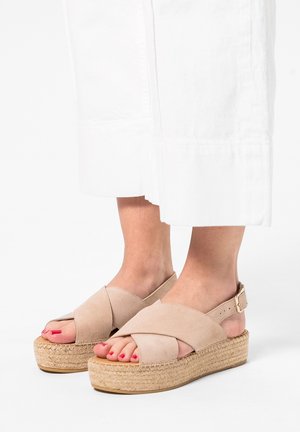 Beige enkelbandje platform sandalen met een kruisbandontwerp, gemaakt van zachte suède, met een natuurlijke geweven jute zool en een lichtbruine rubberen basis.
