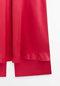 Jupe en satin rouge avec une texture lisse, présentant un ourlet avec un léger éclat et un design superposé en bas.