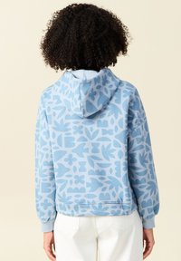 Un hoodie azzurro chiaro presenta un motivo floreale e geometrico, realizzato in un tessuto morbido con una vestibilità comoda e un cappuccio regolabile.