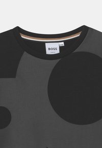 Korte mouw zwarte shirt met een ronde halslijn. Kenmerkt zich door grote zwarte en grijze cirkelvormige patronen. Label zegt "BOSS," maat 8-126, slim fit.