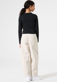 Schwarzes Langarmshirt und beigefarbene, weit geschnittene Hose aus weichem Stoff, kombiniert mit weißen Sneakers. Schlichtes Design ohne Muster.