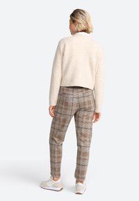 Heller, flauschiger, gekürzter Pullover kombiniert mit braunen Karohosen und hellen Turnschuhen, die Textur und eine strukturierte Passform zeigen.