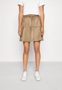 Jupe marron en suédine avec un design à volants et une taille élastique, associée à un t-shirt blanc uni et des baskets blanches.