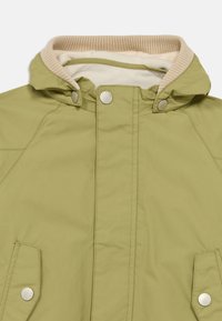 Oljčno zelena jakna s kapuco, kremasto notranjo podlogo, rebrastim ovratnikom in srebrnimi gumbi na pritrditev. Sprednji žepi z neopaznimi gumbi za zapiranje.