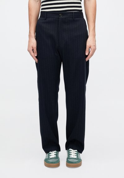 Pantalons rayés bleu marine en tissu texturé, dotés d'une fermeture à bouton et de poches latérales, associés à des baskets vertes.