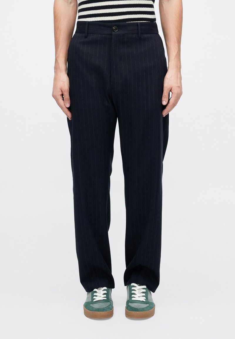 Pantaloni a righe navali realizzati in tessuto testurizzato, con chiusura a bottoni e tasche laterali, abbinati a sneaker verdi.