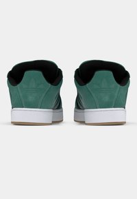 Πράσινα σουέντ αθλητικά παπούτσια με μαύρο εσωτερικό, λευκή σόλα και καφέ εξωτερική σόλα. Διαθέτουν τρεις μαύρες ρίγες και λογότυπο στη φτέρνα.