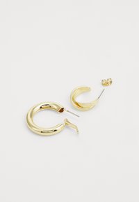 Brincos em forma de argola em tom dourado, disponíveis em tamanhos variados, com uma superfície lisa e polida, design elegante e arredondado, e um fecho seguro.