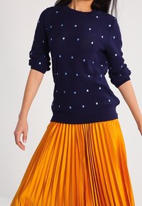 Marinblå stickad tröja med ljusblåa prickar, matchad med en livfull orange plisserad kjol. Fokusera på textur och färgkontrast.