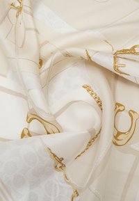 Silkeblød tørklæde i beige med gyldent kædemønster, der har en glat tekstur og elegant fald, som viser detaljeret design.