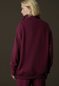 Bordowy, oversize'owy sweatshirt z wysokim kołnierzem, prążkowanymi mankietami i dołem, o gładkiej fakturze i luźnym kroju.