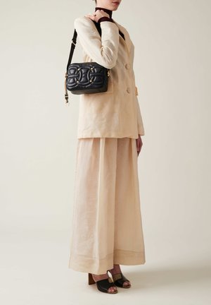 Borsa a spalla nera trapuntata con dettagli in oro. Abbinata a un blazer oversize beige e una gonna fluida, crea un look a strati.