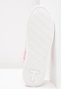 Semelle de basket blanche en caoutchouc texturé, présentant un motif de lignes entrelacées. Le côté est décoré d'un motif floral rose.