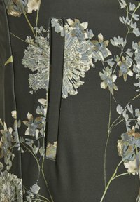 Tissu noir avec un motif floral dans des tons de bleu, gris et beige ; présente un détail de couture visible et une texture douce et lisse.