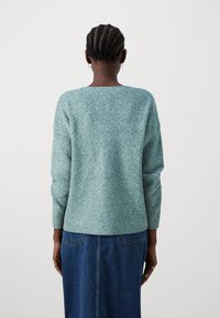 Απαλό μπλε πλεκτό πουλόβερ με φαρδύ λαιμόκοψη, μακριά μανίκια και ραβδωτά μανίκια, συνδυασμένο με τζιν φούστα. Καθαρή υφή και χαλαρή γραμμή.