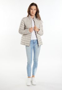 Lichtgrijze gewatteerde jas met een staande kraag, rits aan de voorkant, quilted ontwerp en een gladde textuur. Gecombineerd met lichtblauwe skinny jeans en witte sneakers.