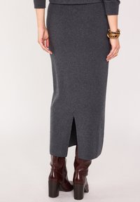 Jupe en tricot grise avec fente à l'arrière, associée à des bottes marron brillantes jusqu'aux genoux. Le tissu semble doux avec une texture lisse.